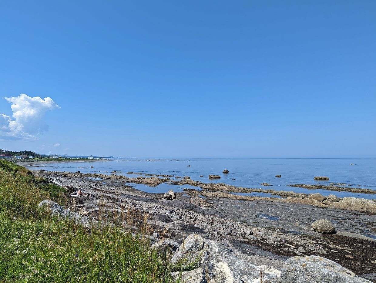 Rocky coast on the Gaspe Peninsula near Matane, with calm ocean and a marina in background