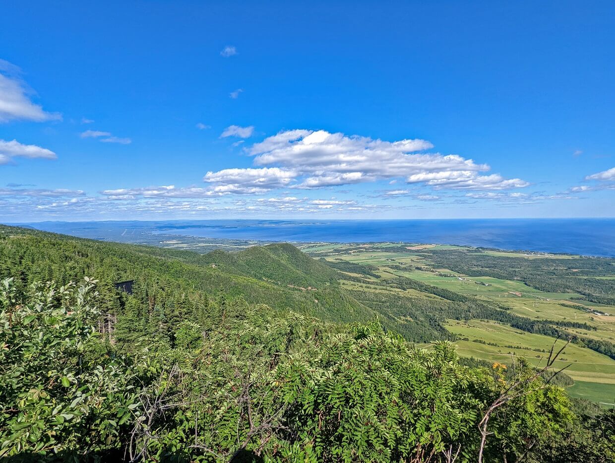 Elevated views looking across forested mountain scenery towards ocean in Gaspe Peninsula, Quebec