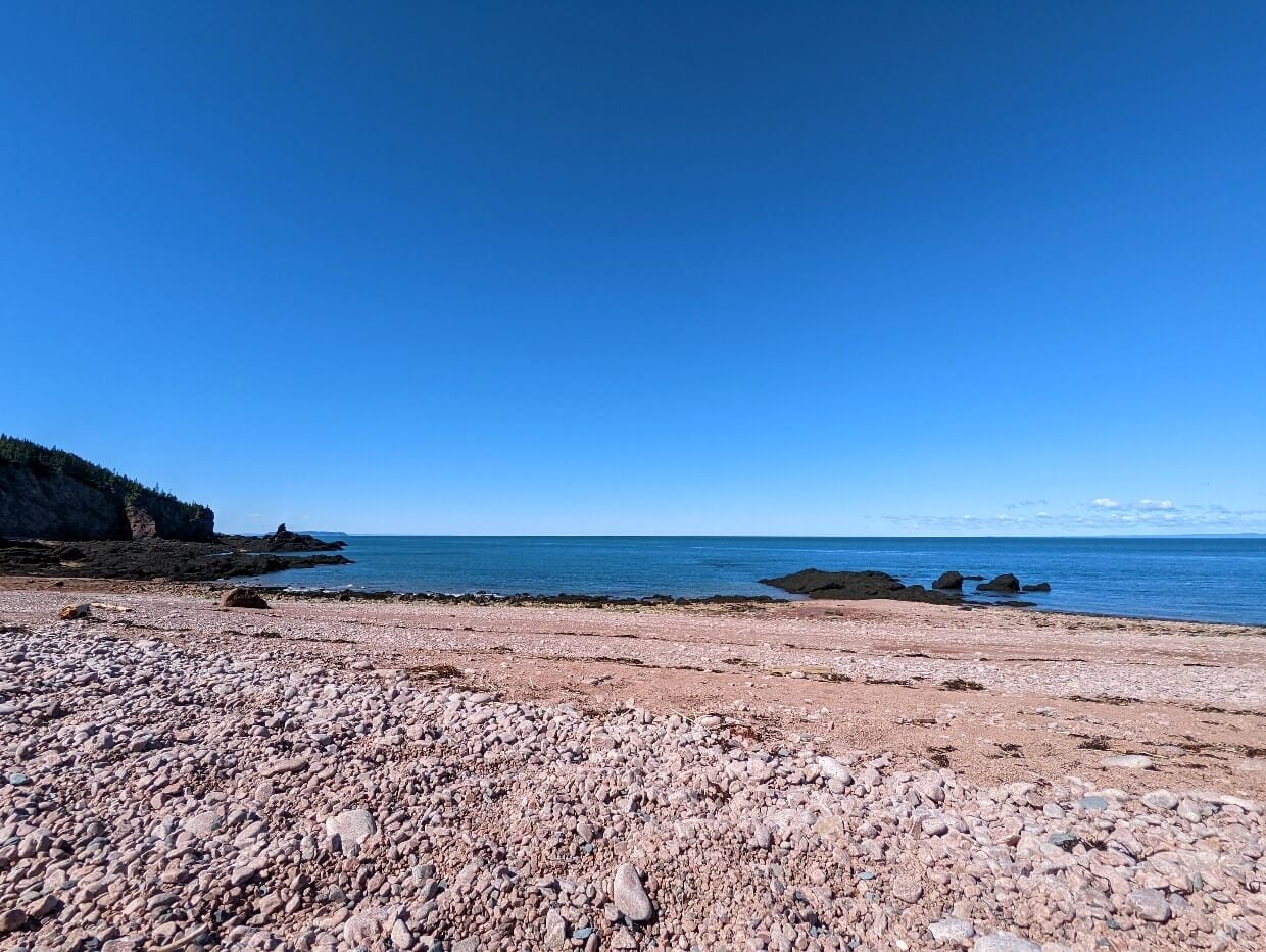 Pink tinged pebble beach at Seal Bay, with rocks just offshore and very calm ocean