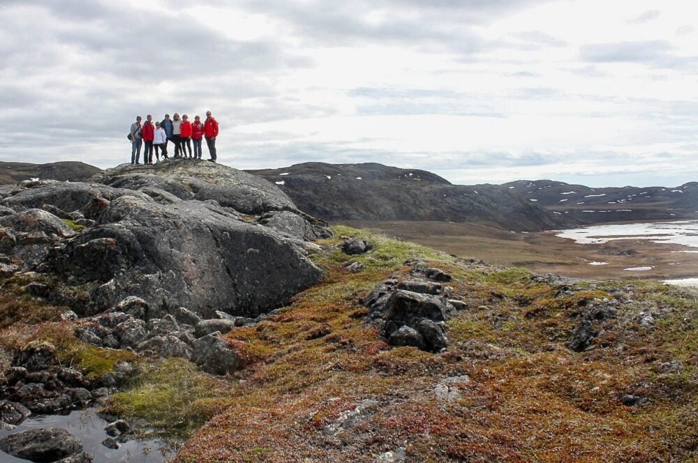 Group of hikers perched on rock with tundra landscape, near Iqaluit, Nunavut