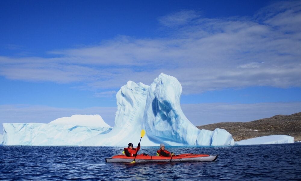 Red kayak with two paddles passing an iceberg near Iqaluit, Nunavut