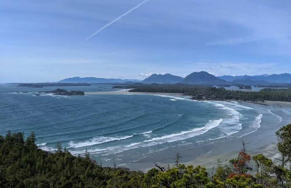 Rolling ocean waves approaching sandy beach, with islands and mountains in background