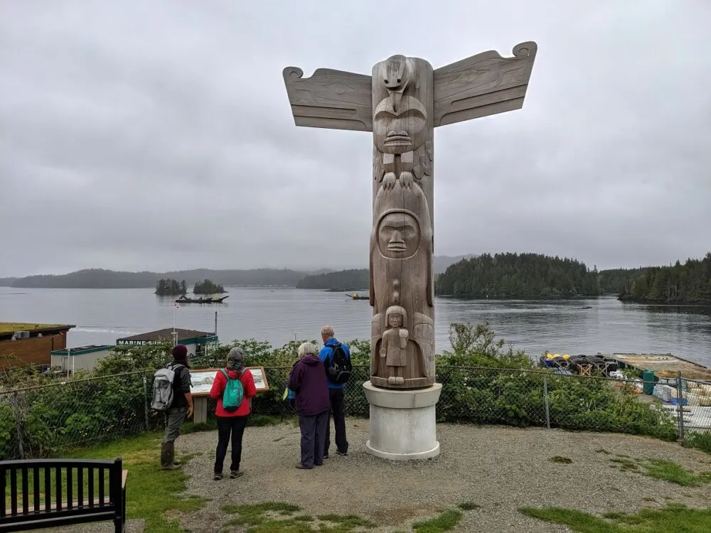 Four people stand close to a carved totem pole in Tofino harbour