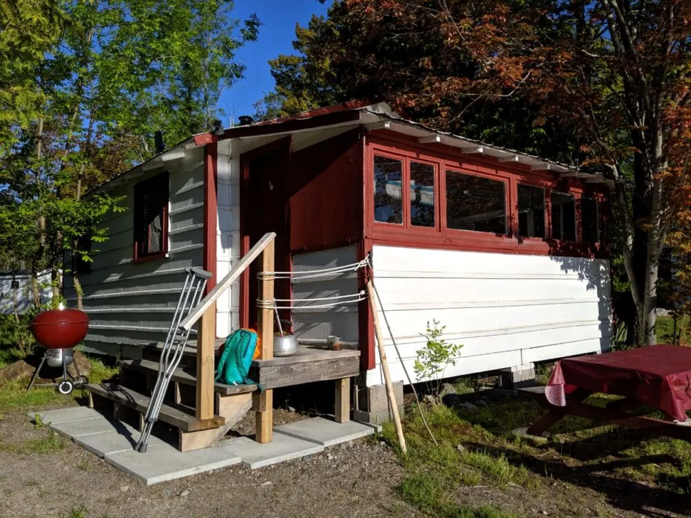 Wooden cottage with steps leading to porch, with red barbecue on the side