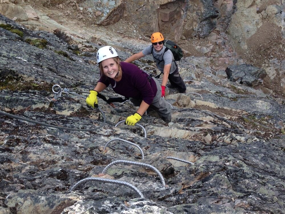 Gemma and JR climbing up a rock wall on the Via Ferrata at Kicking Horse