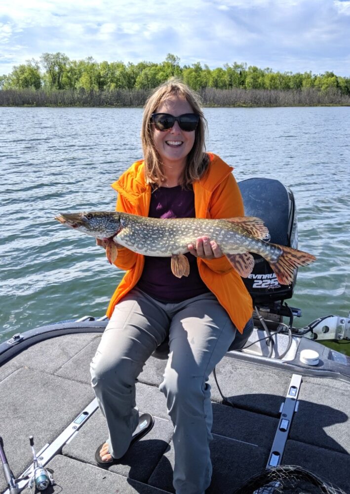 Gemma sat on fishing boat holding large northern pike fish, Lake Huron