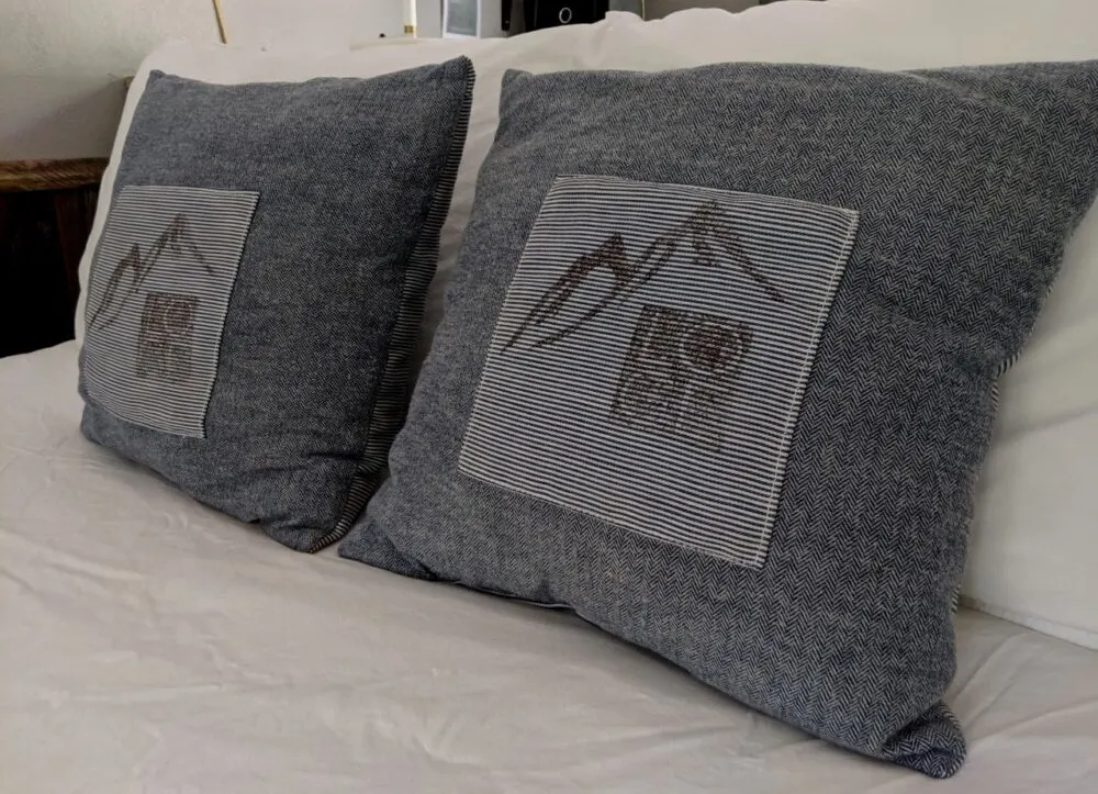 Grey pillows on white linen bed with mountain images, at LOGE Leavenworth