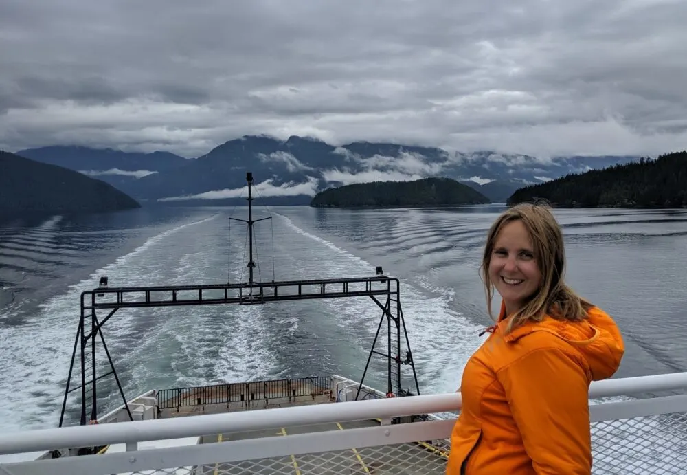 Ferry view travelling between islands and mainland on the Sunshine Coast, with Gemma in orange jacket in foreground, smiling at the camera