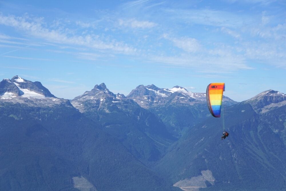 Paraglider flies in font of snow capped mountains