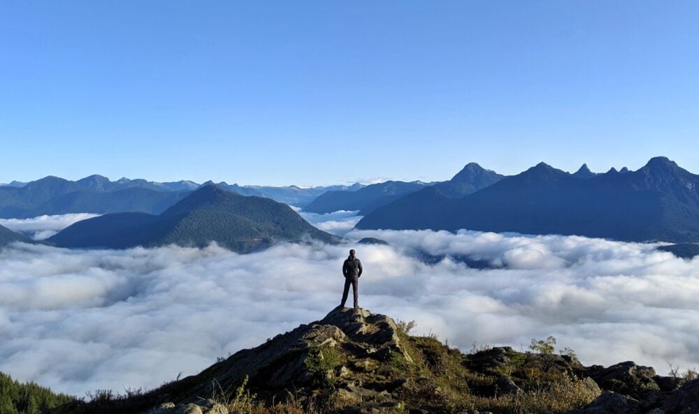 JR on top of mountain, above the clouds surrounded by other peaks