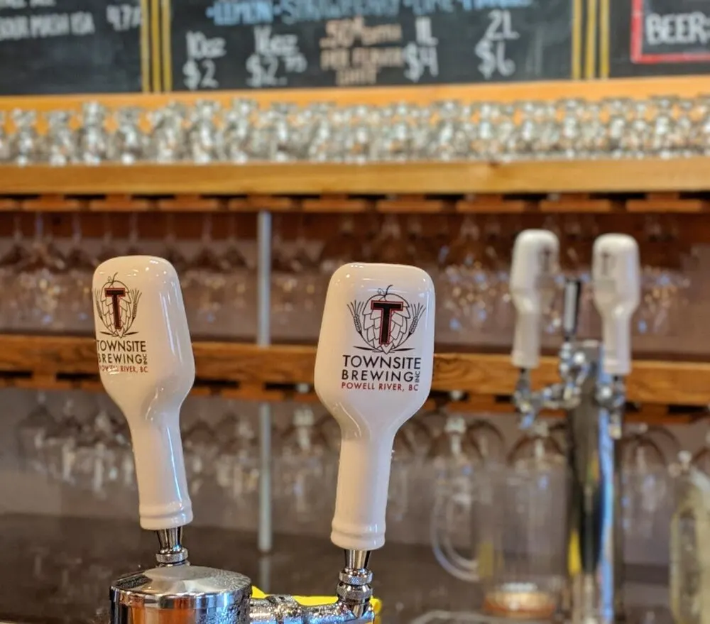 Close up of Townsite Brewing taps at bar, with glasses and blackboard visible behind