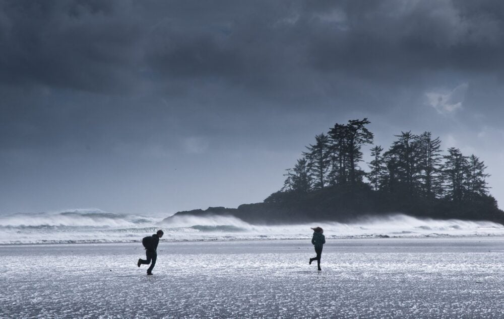 Two people running on a beach with waves crashing behind