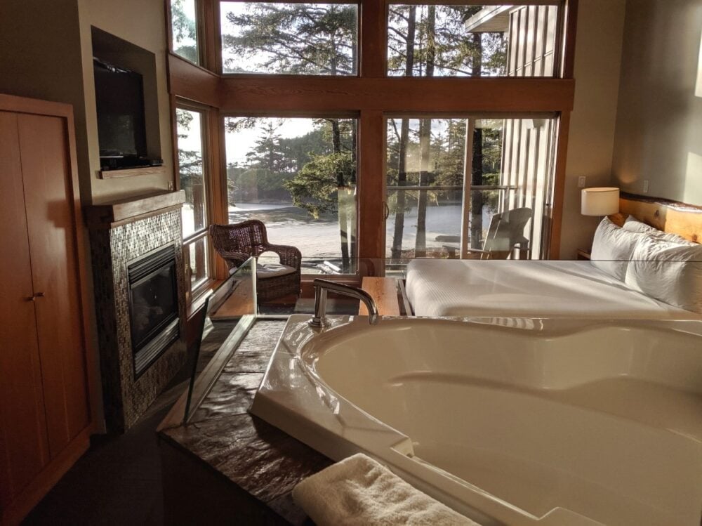 Elevated double soaker tub with king bed and fireplace behind, looking out to beach