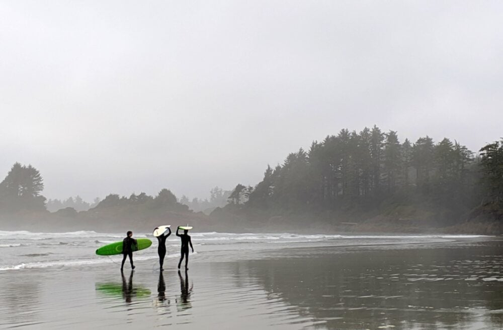 Three surfers walking along the beach in Tofino