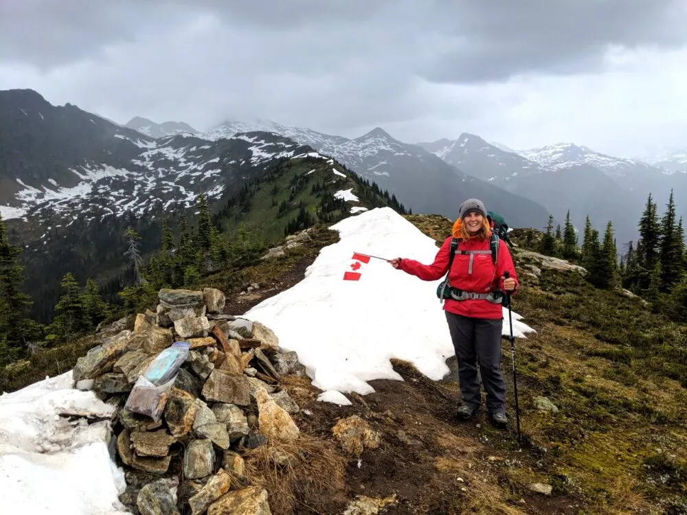 Gemma standing in red jacket next to cairn and snow pile on mountain ridge in Wells Gray Provincial Park