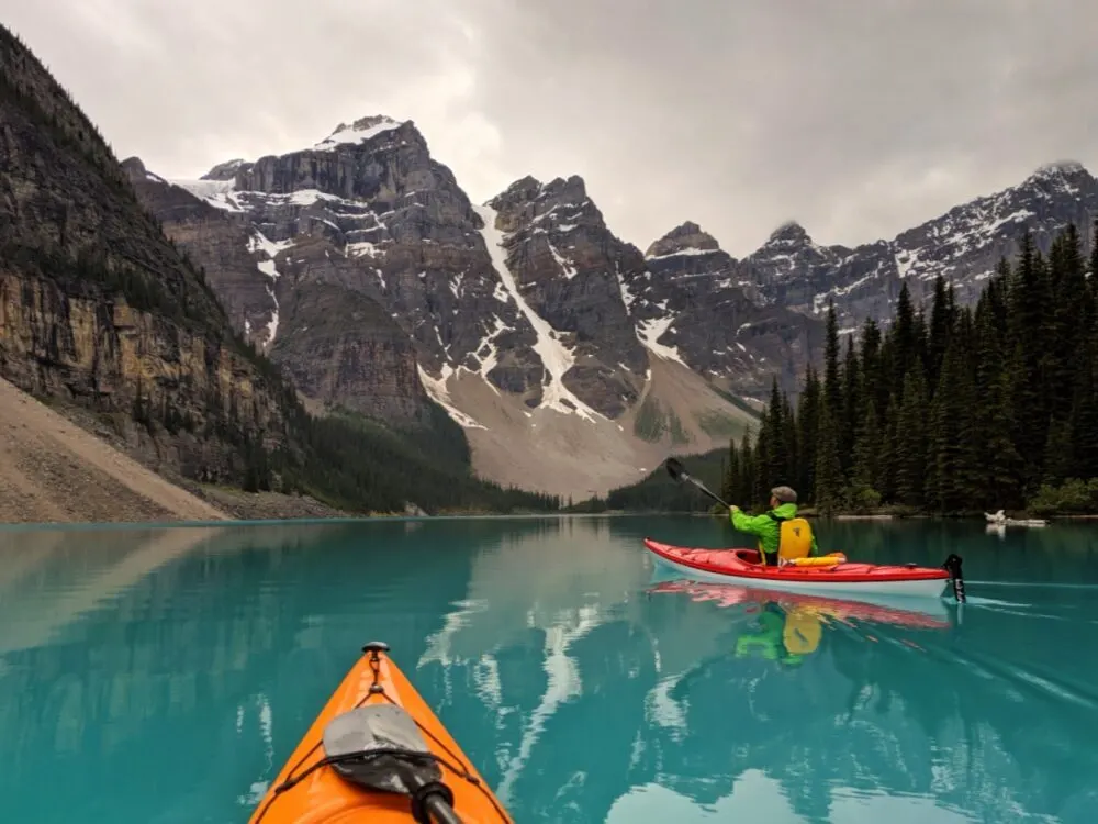 Kayak view of Moraine Lake with reflections of surrounding mountains, with JR in red kayak paddling away from camera