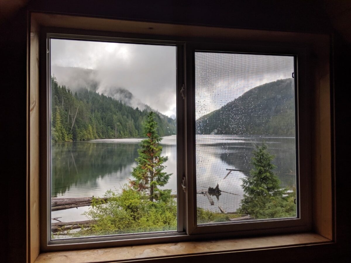 View looking through Confederation Lake hut upstairs window towards still lake and surrounding trees