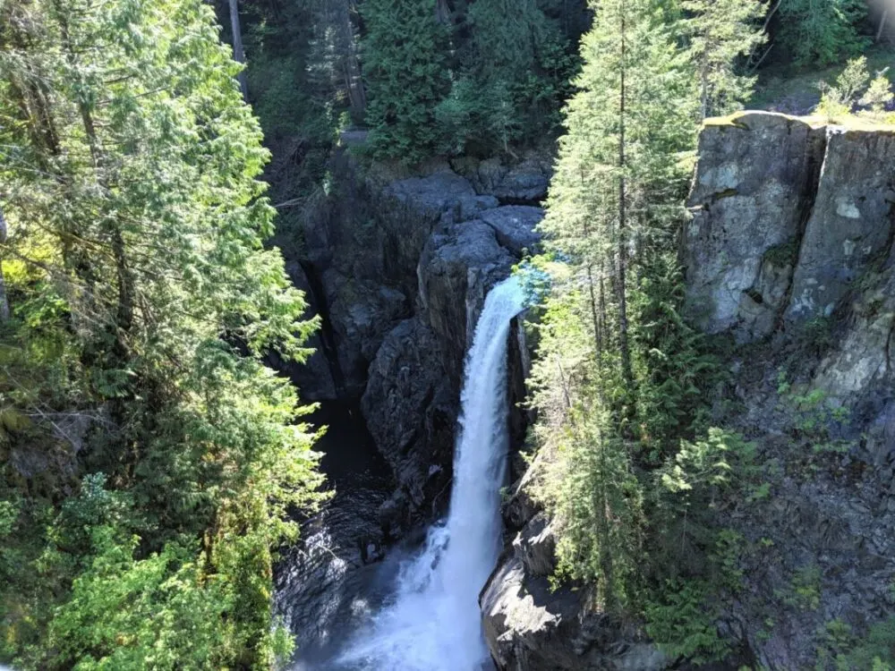 Looking down on huge, cascading Elk Falls, which is falling into a deep rocky canyon. There are overhanging trees on the left