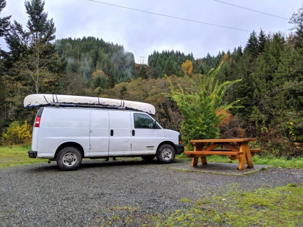 White van parked up next to picnic table with misty forest behind