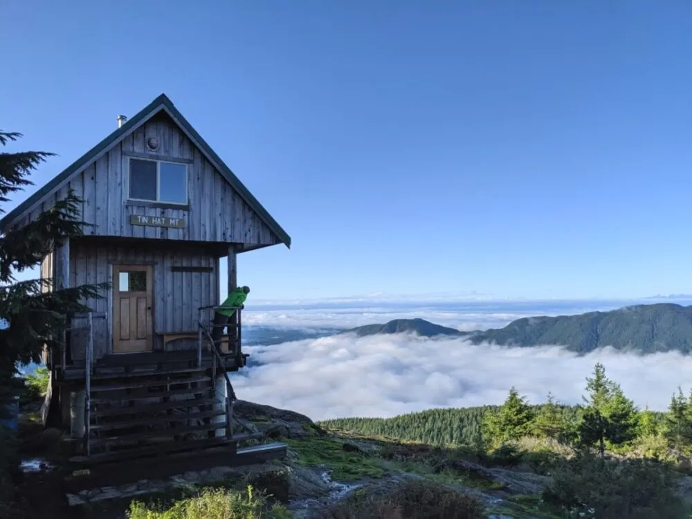 JR standing on the deck of the Tin Hat Mountain hut looking at the cloud covered views