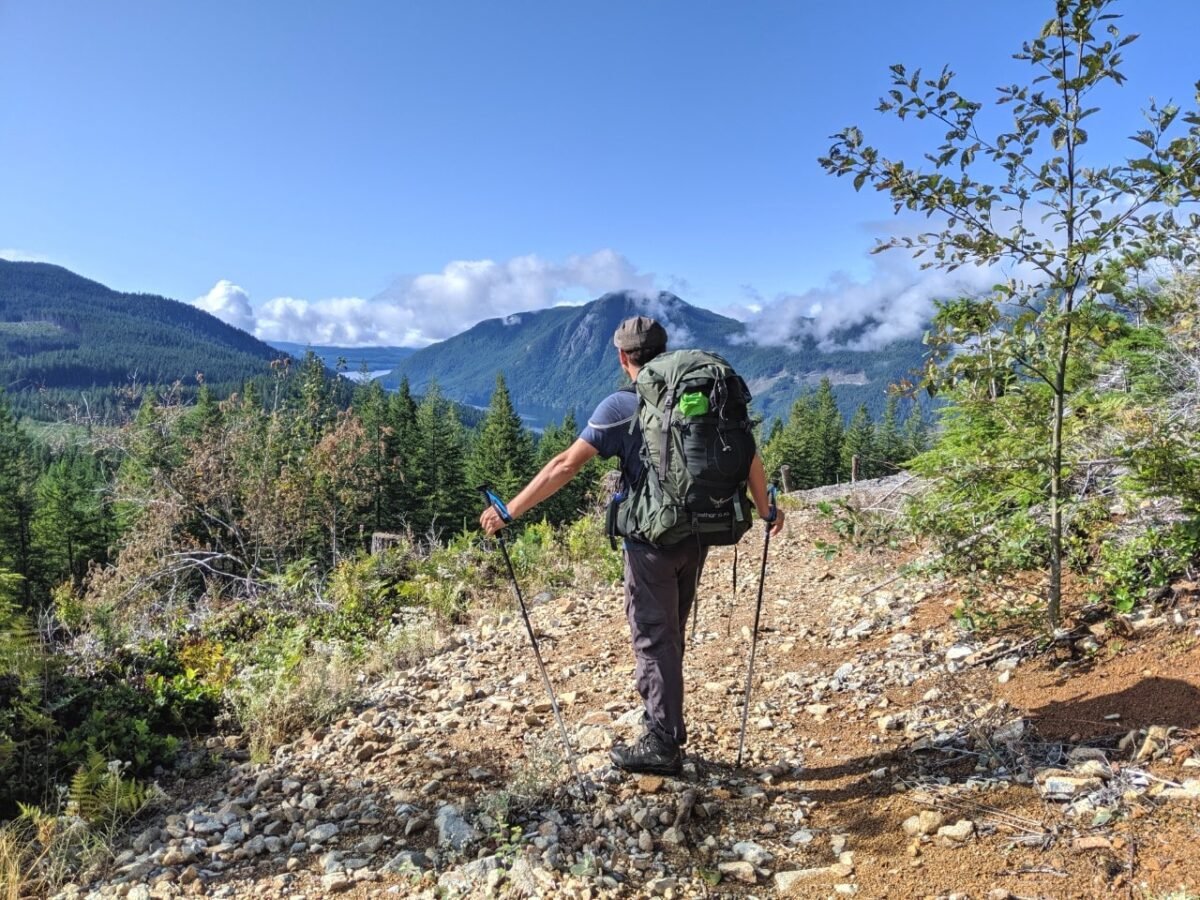 JR standing with two hiking poles looking down at open trail beyond