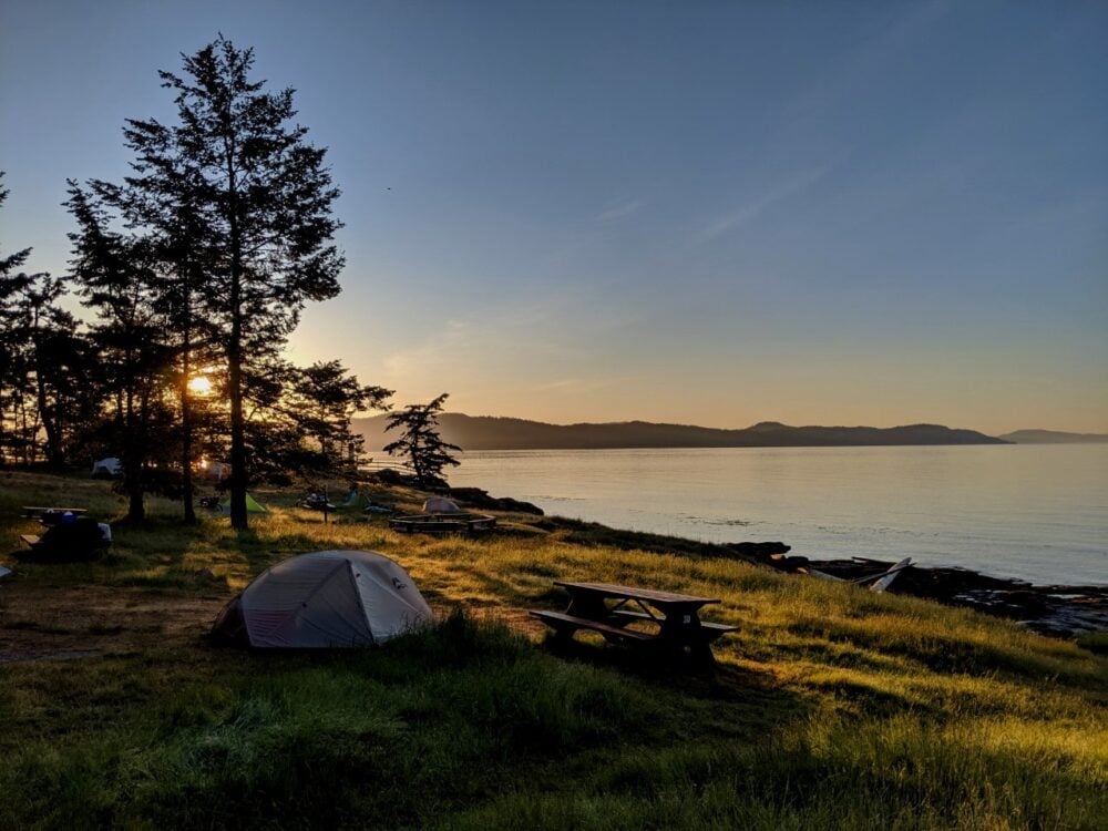 A tent next to a picnic table on a grassy slope in front of the ocean in Ruckle Provincial Park