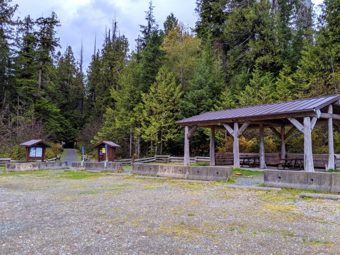 The Cape Scott Provincial Park parking lot with picnic tables covered by a shelter plus outhouse and information board