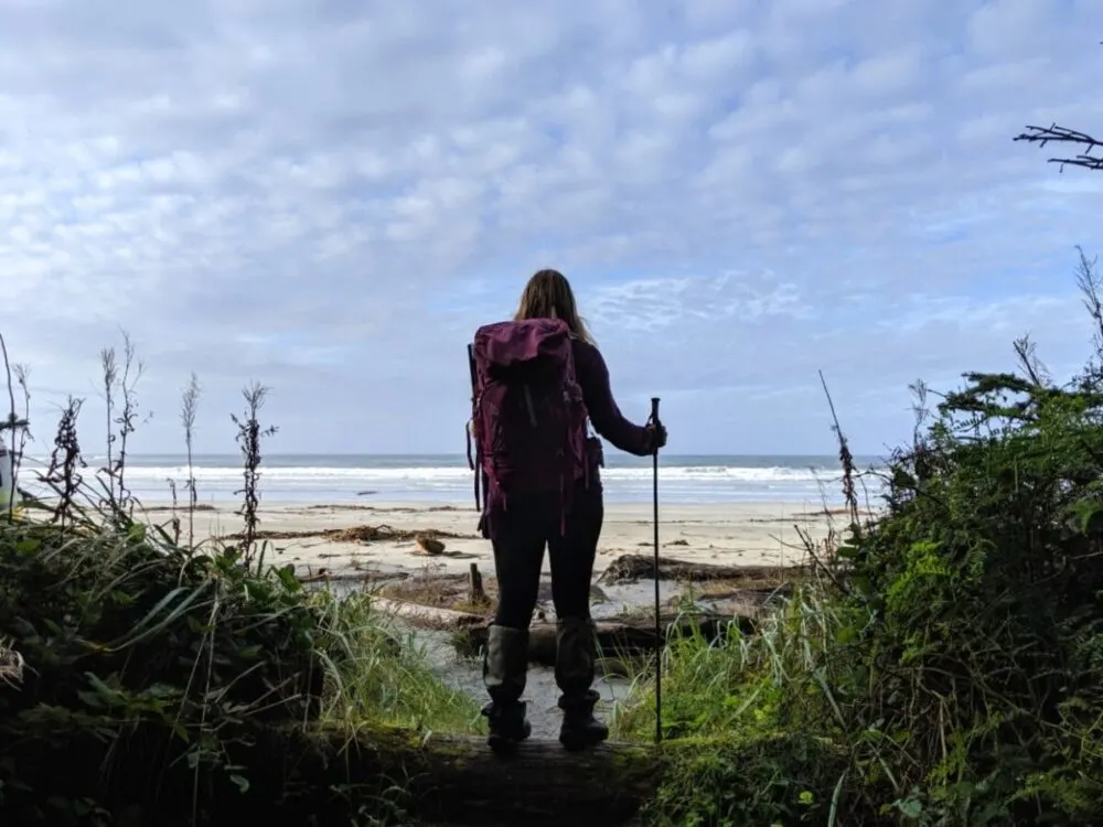 Back view of Gemma standing in front of golden sand beach with ocean in background