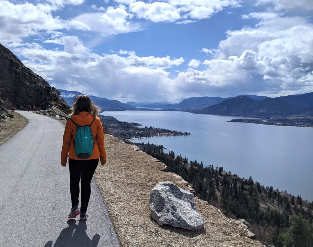 Gemma walking along paved KVR Little Tunnel Trail with elevated views of Okanagan Lake back towards Penticton