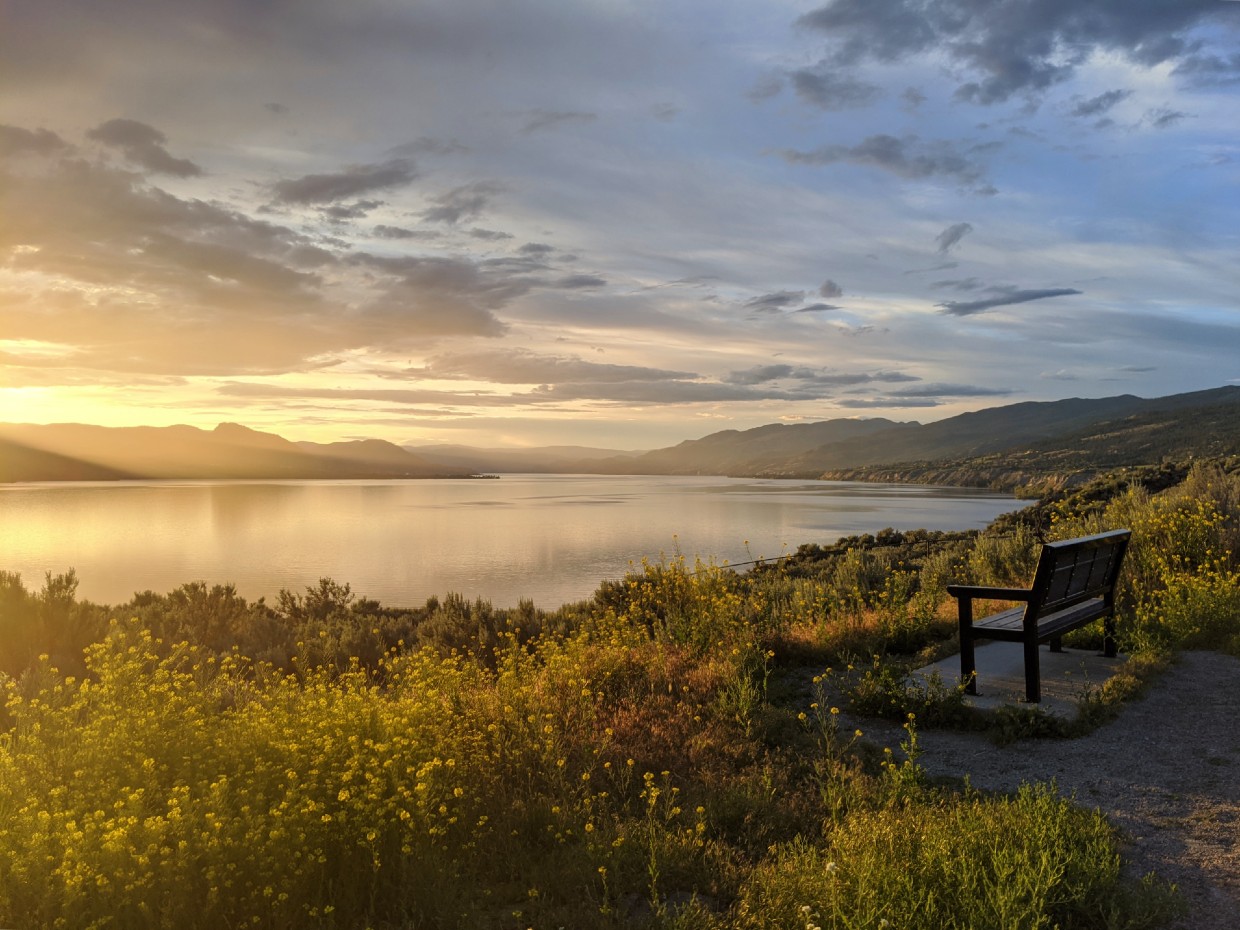 Side view of bench in front of elevated lake view on KVR Trail in Penticton, with sunset