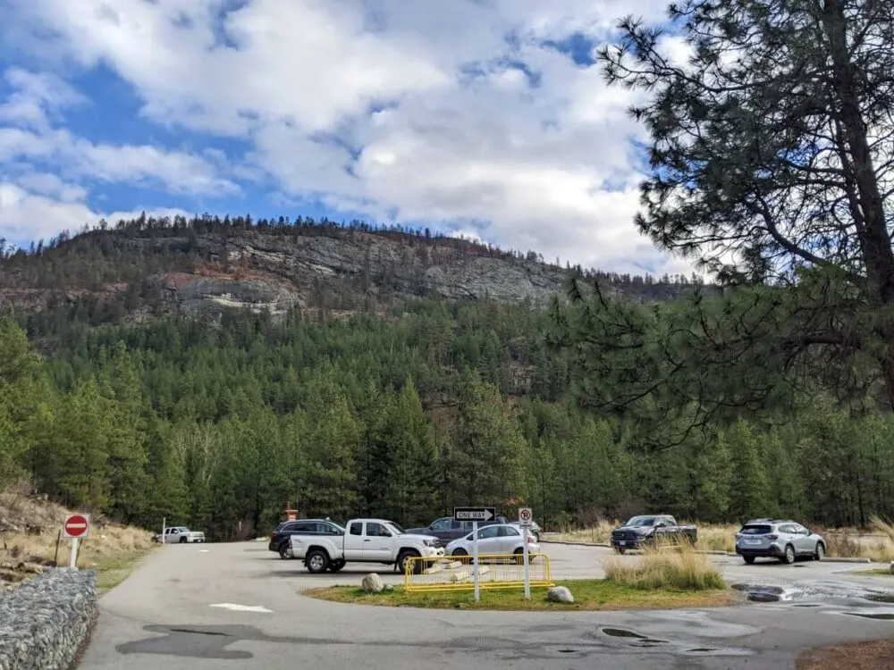 Large cement parking lot with half a dozen parked vehicles, with forest and hills behind