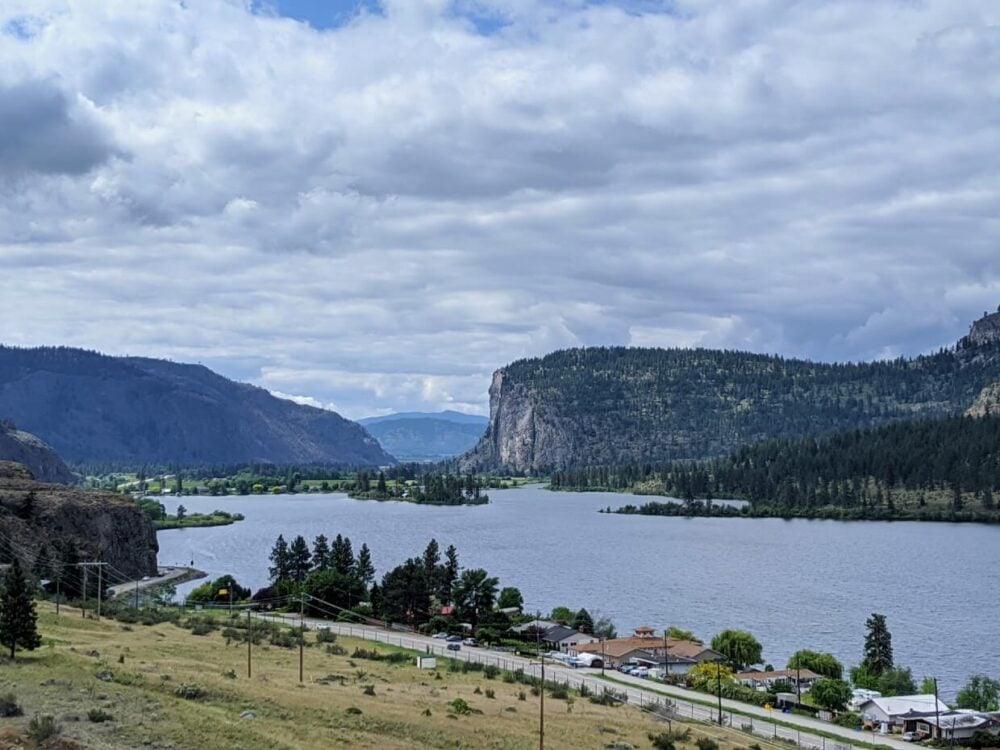 Elevated view looking down on lake with highway on one side, with huge rising bluff in background