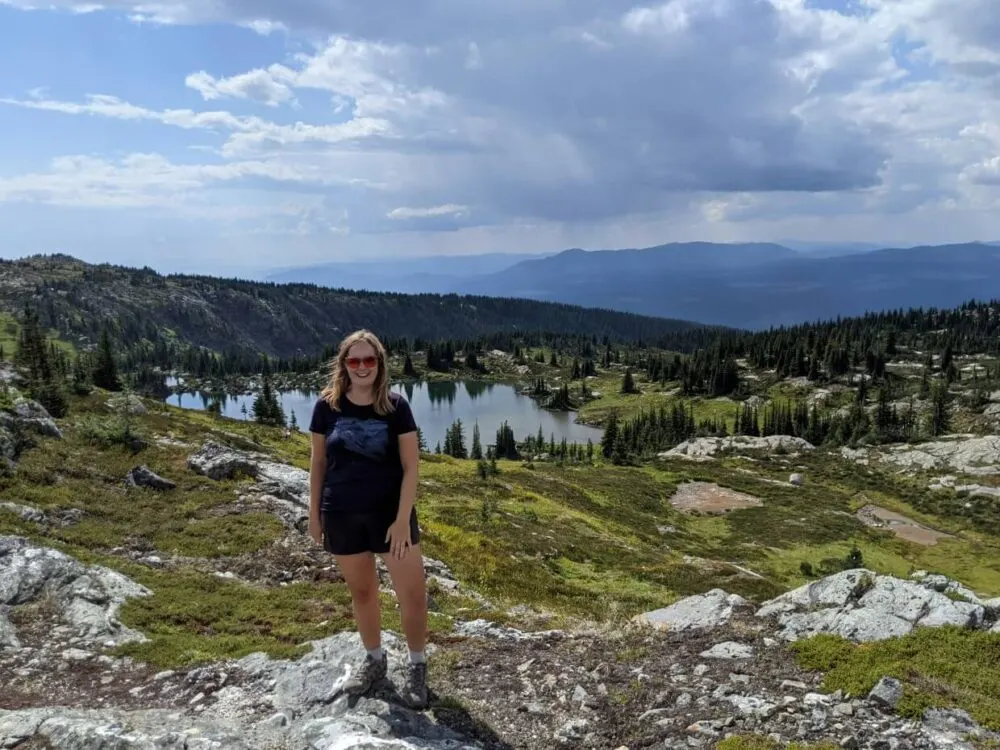 Gemma is standing in front of sub-alpine landscape in Wells Gray Provincial Park, with Sheila Lake below