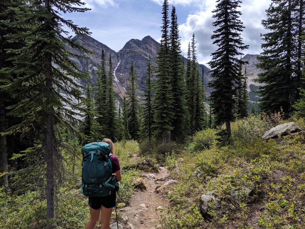 Back view of Gemma hiking with large backpack looking ahead to mountainous hiking trail