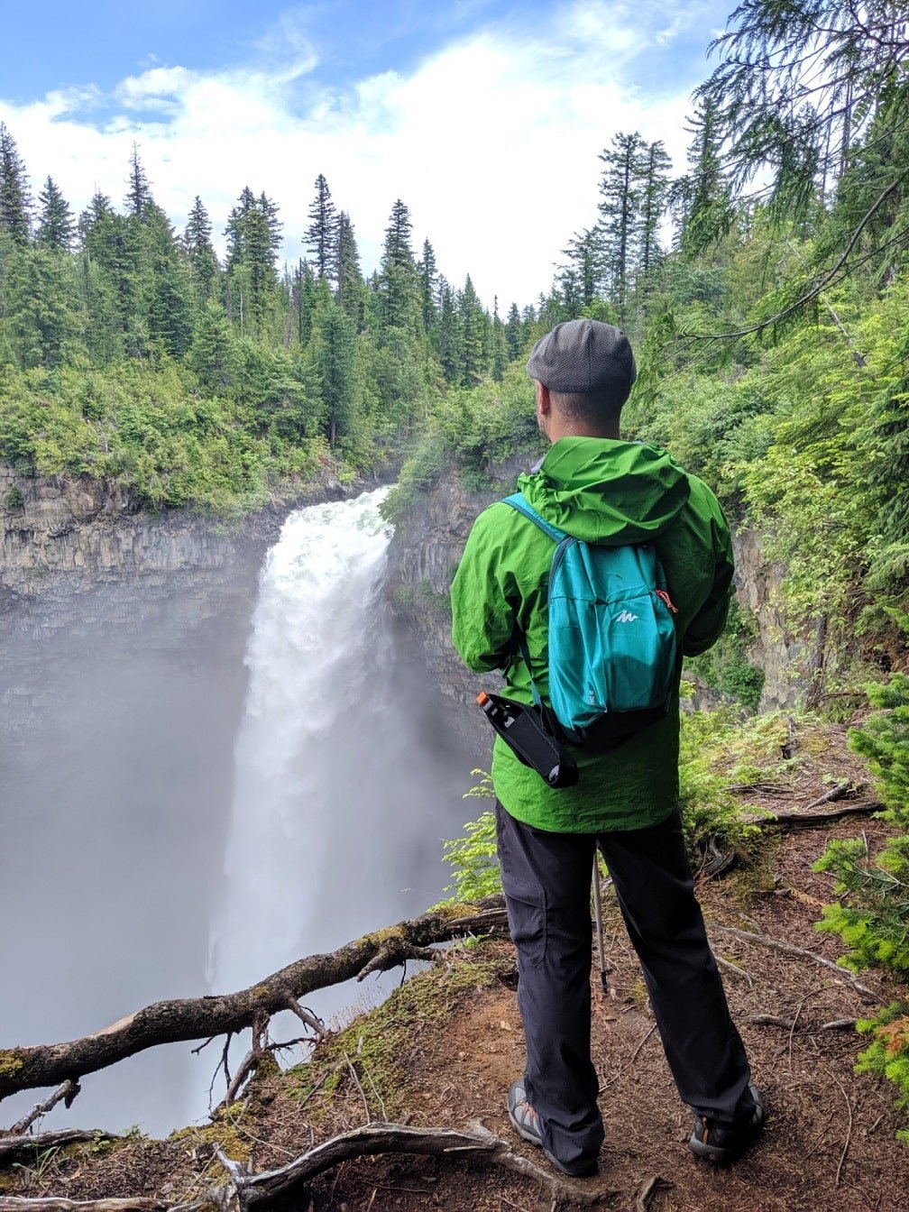 Back view of JR standing in front of Helmcken Falls in a green jacket and green backpack