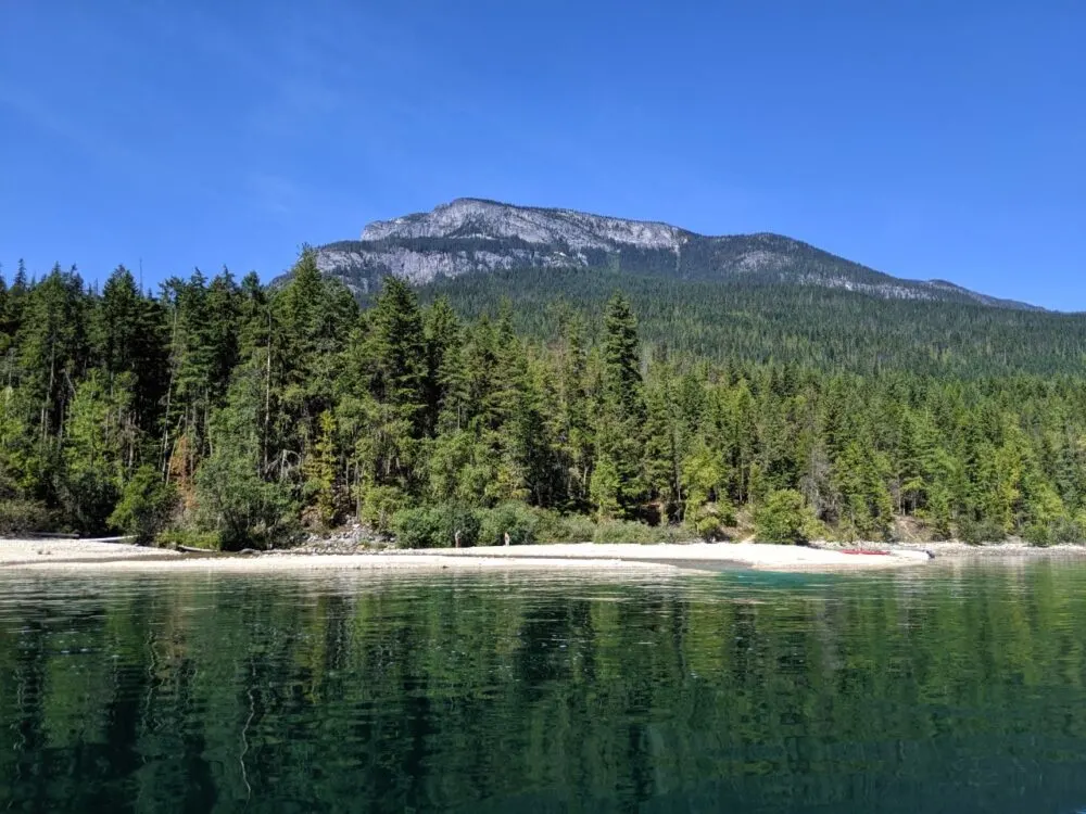 Water view looking over to one of Slocan Lake's golden sand beaches, with a backdrop of forest and mountains