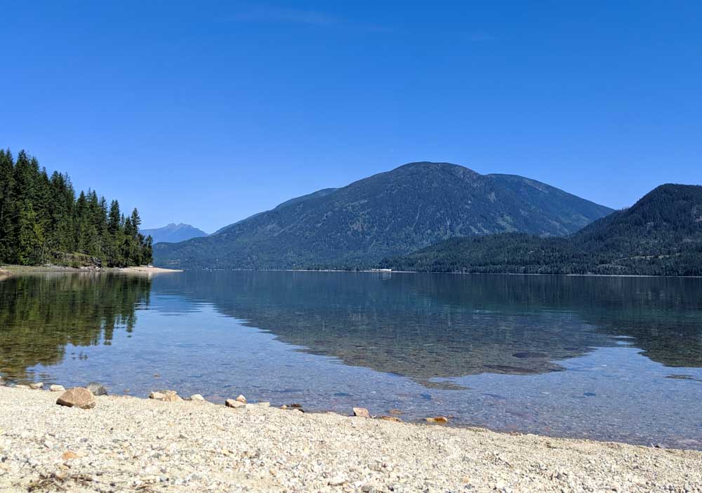 View from sandy beach at Nemo Creek looking out to still lake and mountains beyond