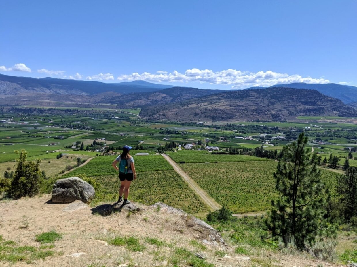Gemma standing on elevated rock platform above vineyards near Osoyoos, BC