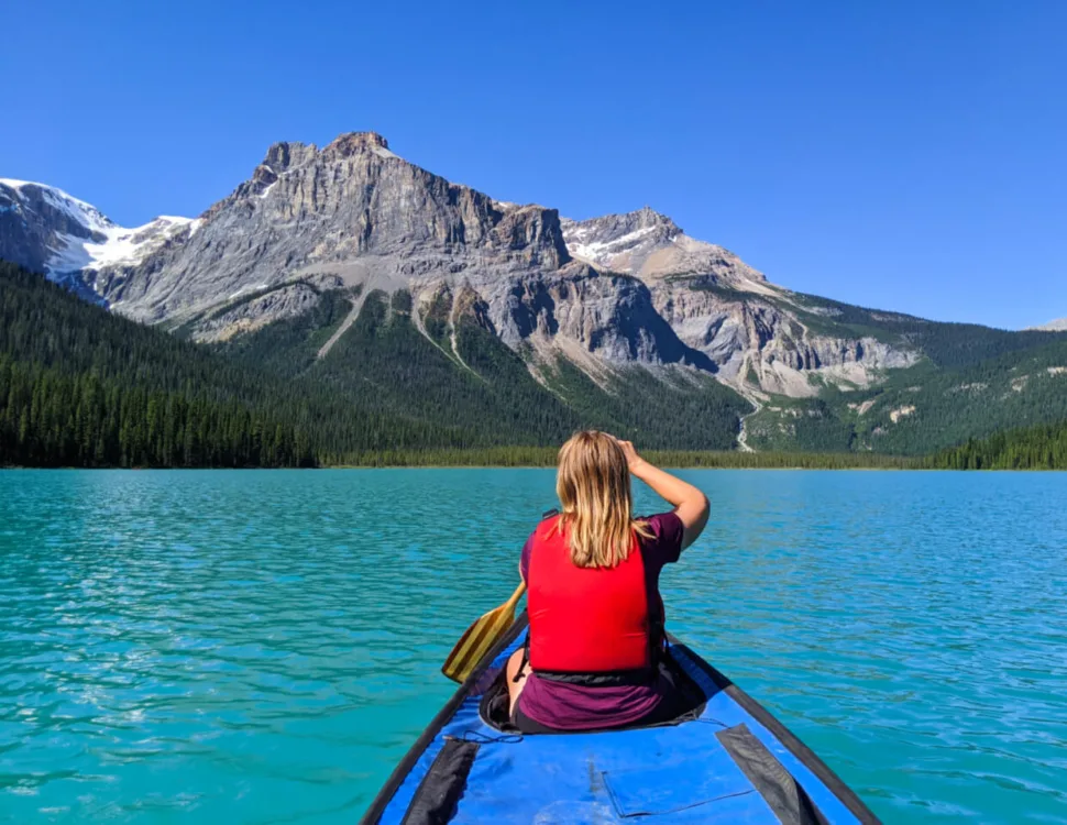 Back view of Gemma sat in canoe paddling on Emerald Lake, with bright turquoise water with mountainous backdrop