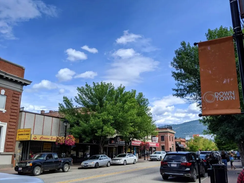 Street view of downtown Vernon with parked cars, shops, trees and orange downtown sign