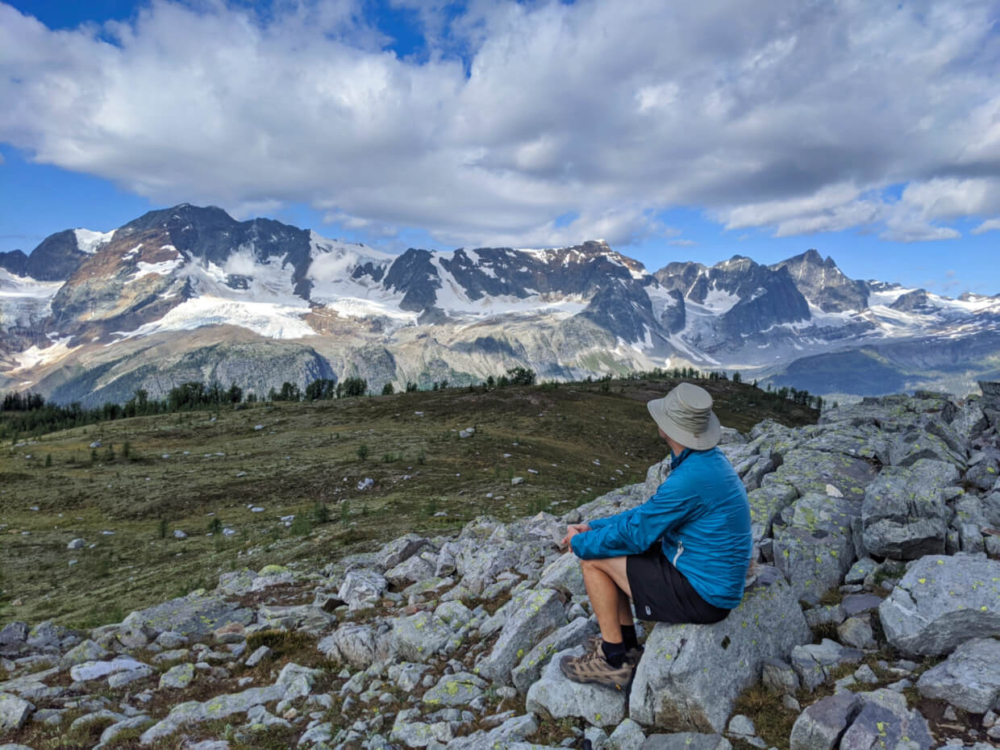 Side/back view of JR sitting down on rock looking out at views of the Macbeth Icefield on the Monica Meadows trail, one of the best BC day hikes