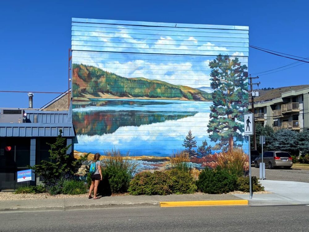 Gemma standing on sidewalk looking up at Kalamalka Lake mural in Vernon, BC