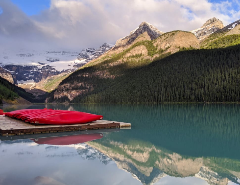 Red canoes rest on a floating platform on Lake Louise, Alberta, a reflective lake with a huge glacier in the background