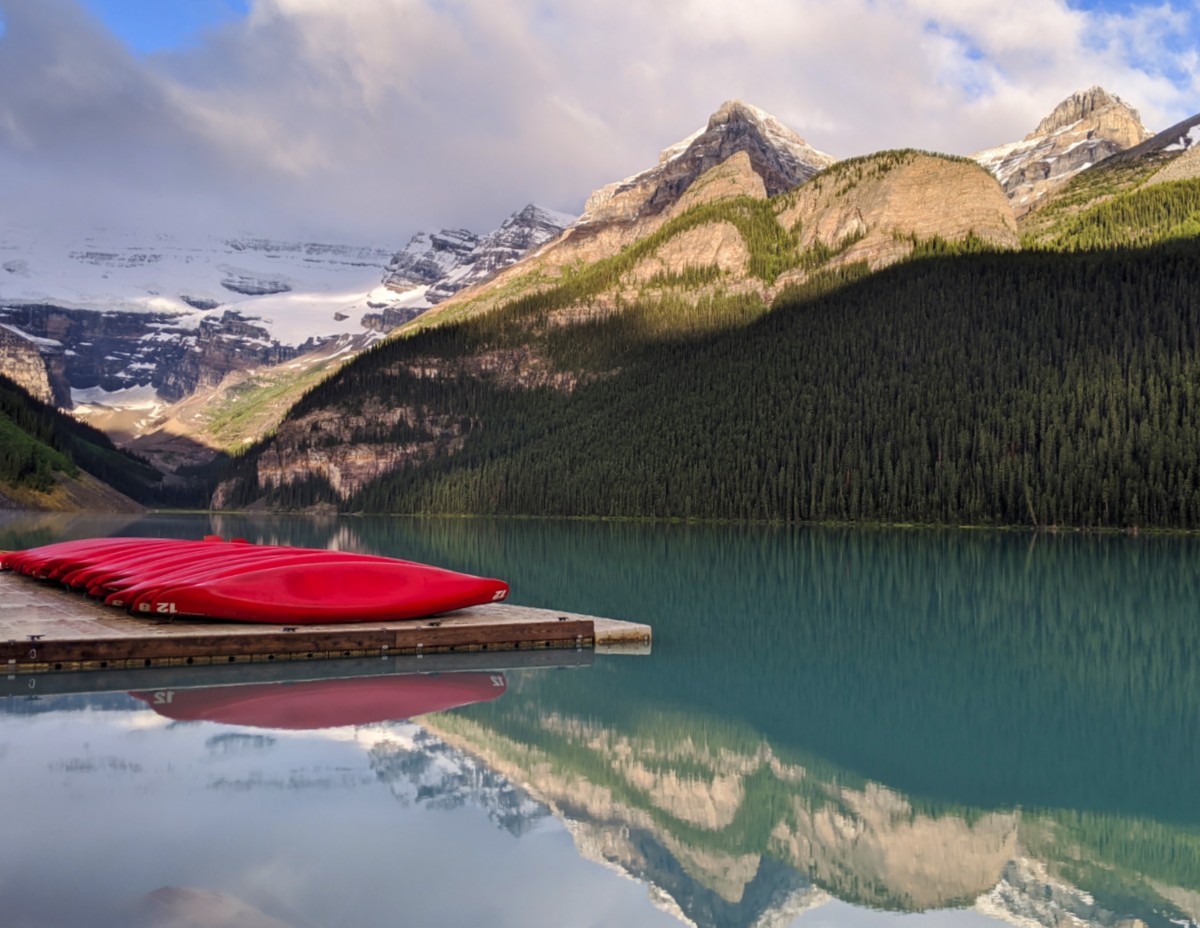 View of Lake Louise from shore with mirror like reflections of surrounding mountains and glacier