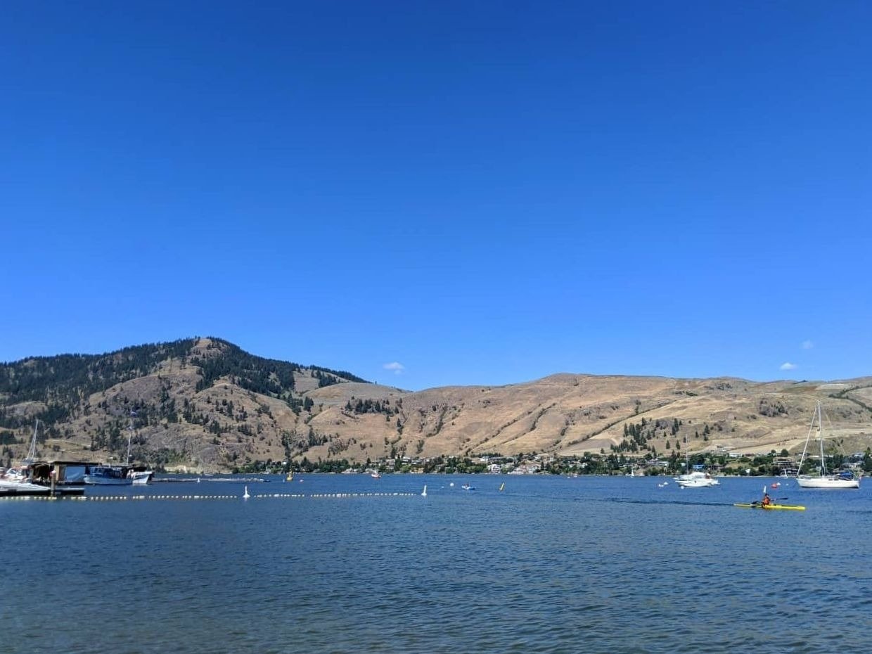 Okanagan Lake view from Paddlewheel beach with kayaker and grassland hills behind