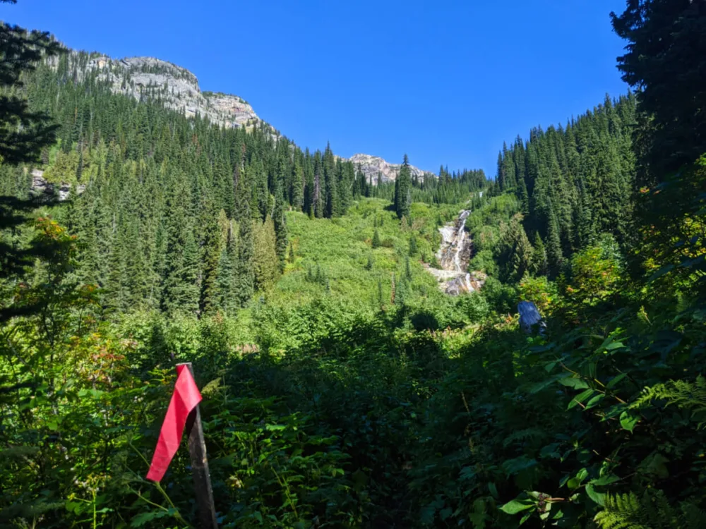 Red flag next to trail with waterfall and snow capped mountain behind