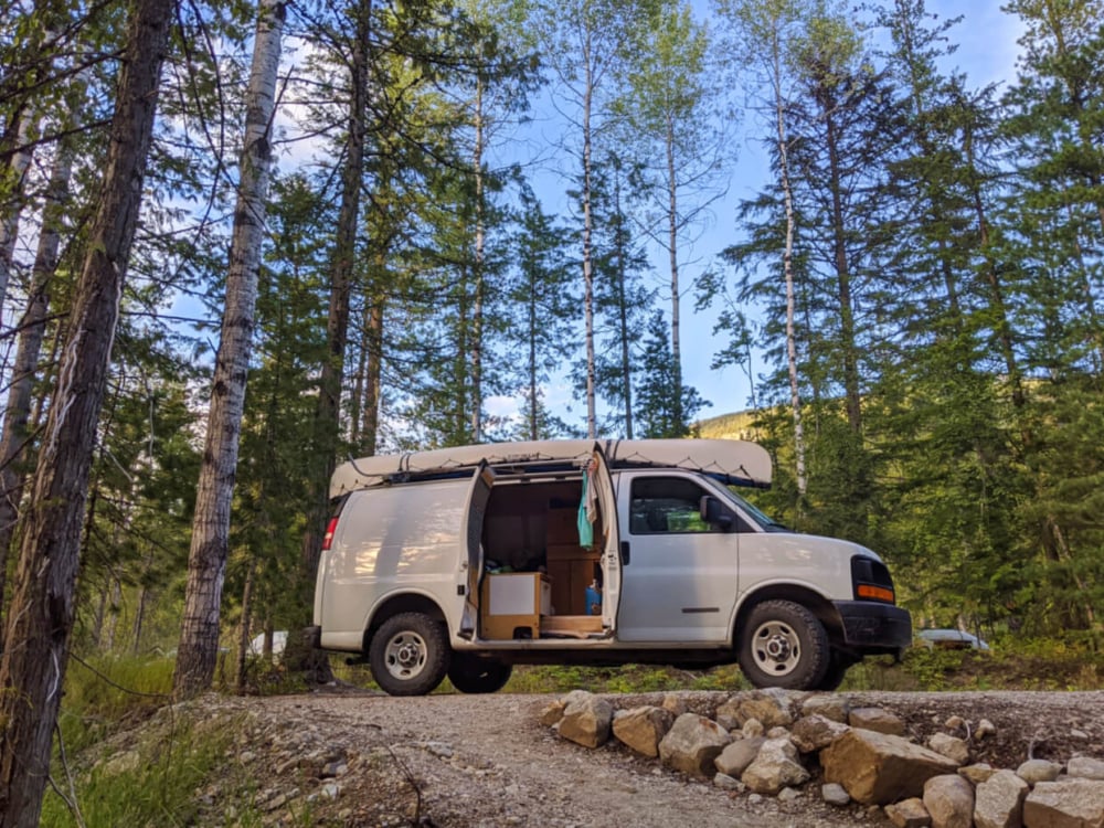 Looking up at white van parked in campground with door open, showing conversion inside