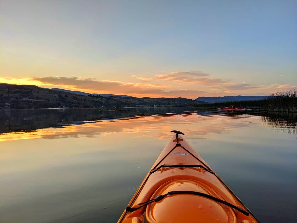 Kayak view of Swan Lake at sunset with orange yellow skies and calm water