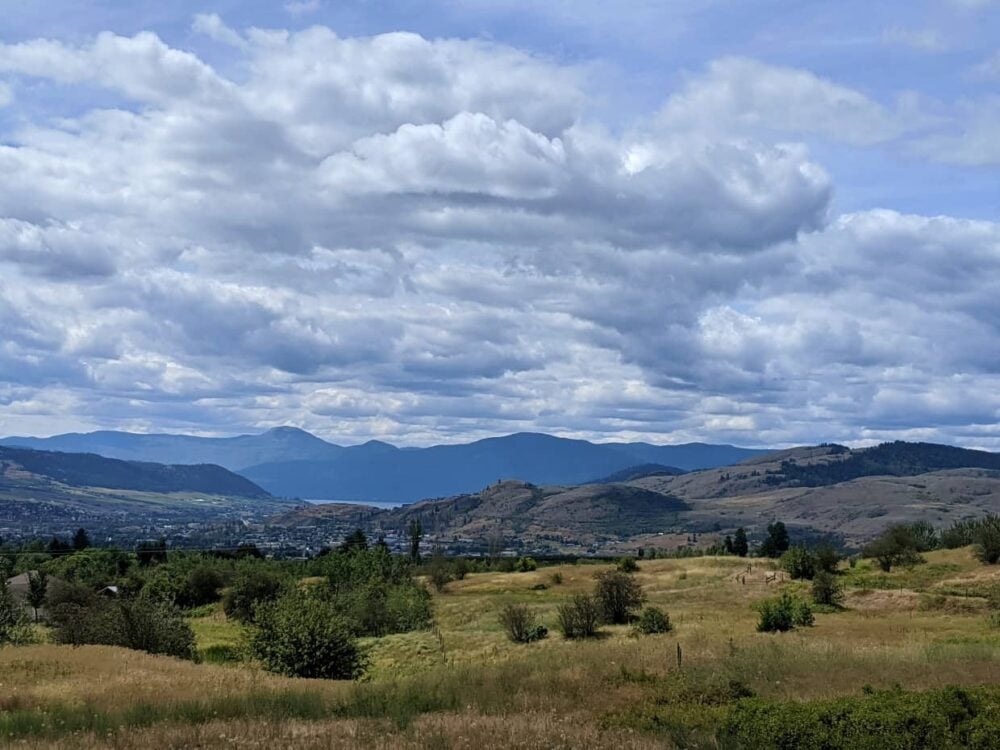 Elevated view looking down towards Vernon with rolling grasslands, mountains and lakeshore