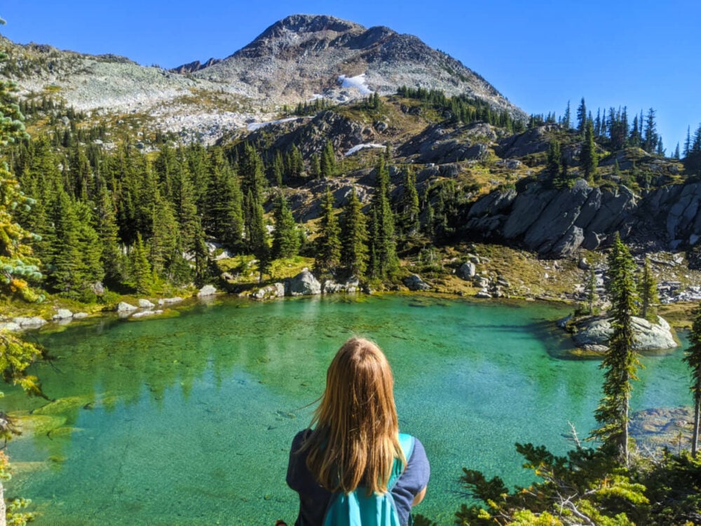 Gemma is sitting in front of turquoise lake, which is backdropped by mountain and ridge